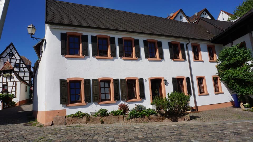 Weiß verputztes Torwächterhaus mit grünen Fensterläden am Kopfsteinpflasterplatz